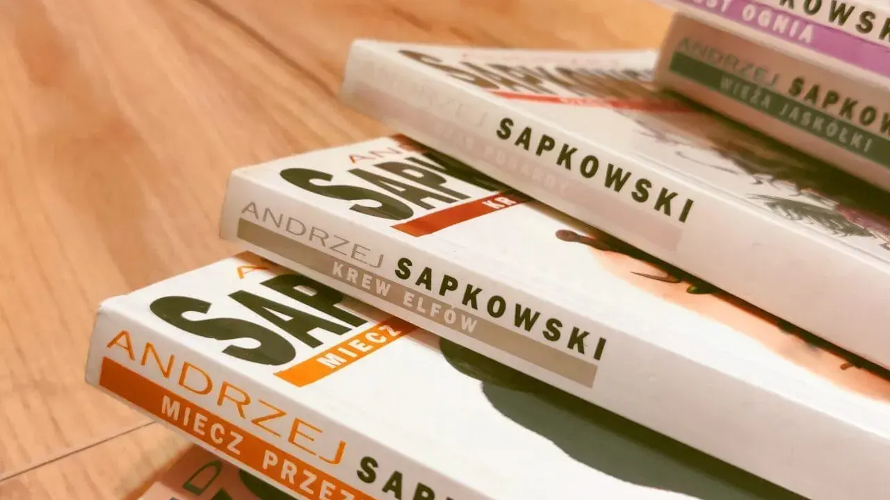 Książki Andrzeja Sapkowskiego ułożone w stos. Widoczne tytuły: "Miecz Przeznaczenia", "Krew Elfów", "Czas Pogardy", "Wieża Jaskółki", "Chrzest Ognia". Idealne do poznania kolejności czytania o wiedźminie.