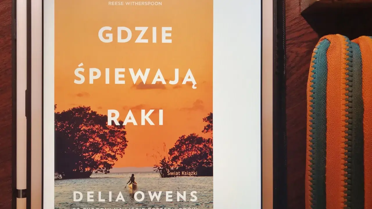 Okładka książki "Gdzie śpiewają raki" z Delia Owens. Na pomarańczowym tle zachodzącego słońca, widać sylwetki drzew i kajakarza na wodzie.
