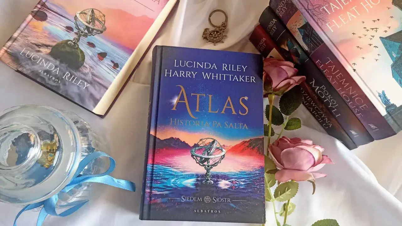 Książka "Atlas. Historia pa Salta" z serii "Siedem sióstr" Lucindy Riley i Harry'ego Whittakera, obok innych tomów cyklu i róż.