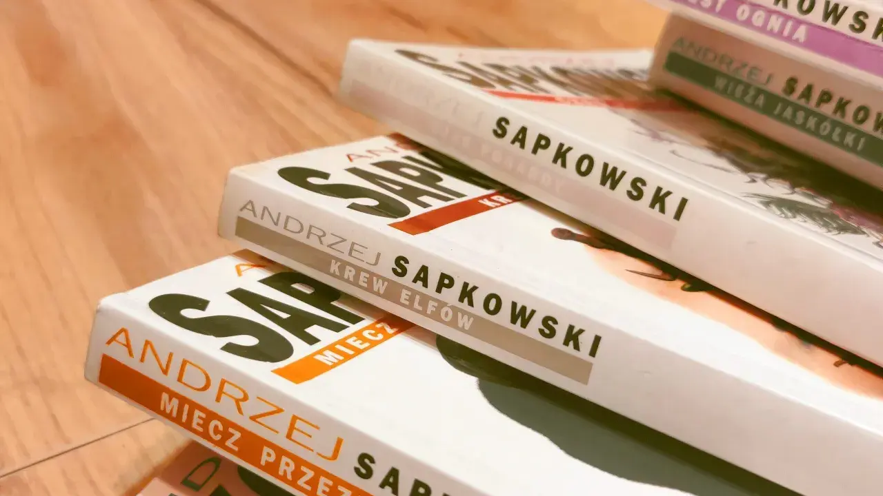 Stos książek Andrzeja Sapkowskiego, w tym "Miecz Przeznaczenia" i "Krew Elfów", gotowy do podróży po świecie Wiedźmina.