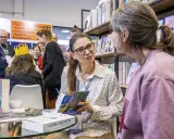 Ałbena Grabowska rozmawia z czytelniczką przy stoisku z książkami. W tle widać innych ludzi i półki z publikacjami.