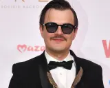 Dawid Ogrodnik w garniturze i okularach, z wąsami, trzyma statuetkę. W tle napisy "Polskie Nagrody" i "Viva!".