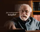 Uśmiechnięty starszy pan w okularach, otoczony regałami pełnymi książek, zastanawia się nad tym, jak katalogować książki.
