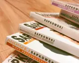 Stos książek Andrzeja Sapkowskiego, w tym "Miecz Przeznaczenia" i "Krew Elfów", gotowy do podróży po świecie Wiedźmina.