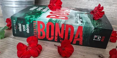 Katarzyna Bonda, autorka serii z Huberta Meyerem, na tle czerwonych kwiatów.