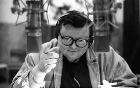 Wojciech Mann w młodości, w słuchawkach i okularach, wskazuje palcem, gotowy do nagrania.