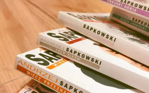 Stos książek Andrzeja Sapkowskiego, w tym "Miecz Przeznaczenia" i "Krew Elfów", gotowy do podróży po świecie Wiedźmina.