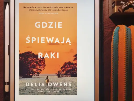 Okładka książki "Gdzie śpiewają raki" z Delia Owens. Na pomarańczowym tle zachodzącego słońca, widać sylwetki drzew i kajakarza na wodzie.