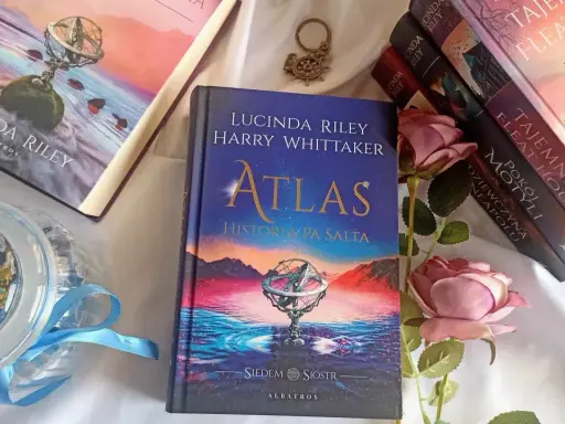 Książka "Atlas. Historia pa Salta" z serii "Siedem sióstr" Lucindy Riley i Harry'ego Whittakera, obok innych tomów cyklu i róż.