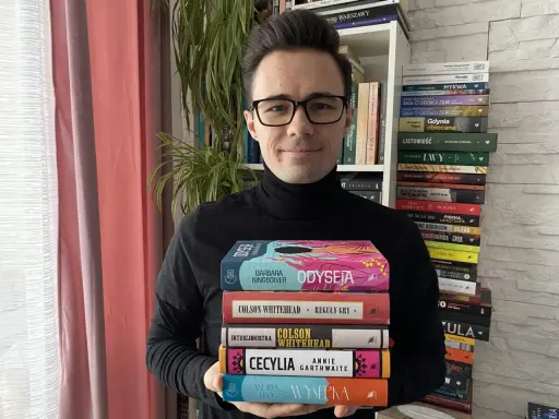 Mężczyzna trzyma stos książek, wśród nich "100 najlepszych książek wg magazynu Time".