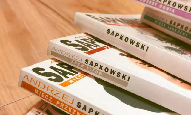 Książki Andrzeja Sapkowskiego ułożone w stos. Widoczne tytuły: "Miecz Przeznaczenia", "Krew Elfów", "Czas Pogardy", "Wieża Jaskółki", "Chrzest Ognia". Idealne do poznania kolejności czytania o wiedźminie.