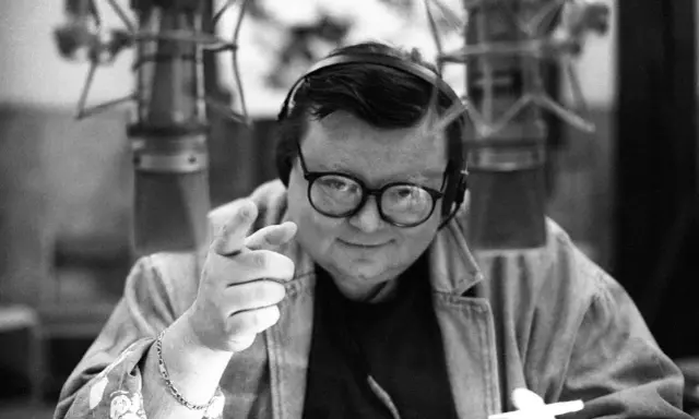 Wojciech Mann w młodości, w słuchawkach i okularach, wskazuje palcem, gotowy do nagrania.