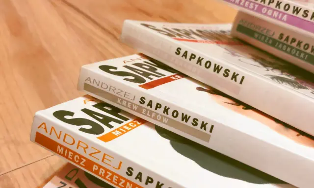 Stos książek Andrzeja Sapkowskiego, w tym "Miecz Przeznaczenia" i "Krew Elfów", gotowy do podróży po świecie Wiedźmina.