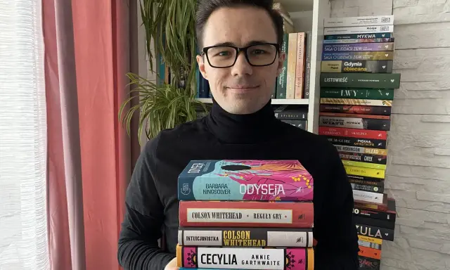 Mężczyzna trzyma stos książek, wśród nich "100 najlepszych książek wg magazynu Time".