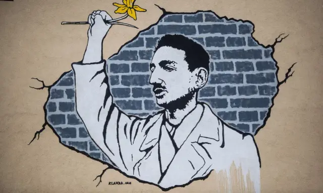 Mural przedstawia mężczyznę z żółtym kwiatem, który przebija się przez ceglaną ścianę. Jakby chciał zdążyć przed panem bogiem, by wręczyć mu ten symbol nadziei.
