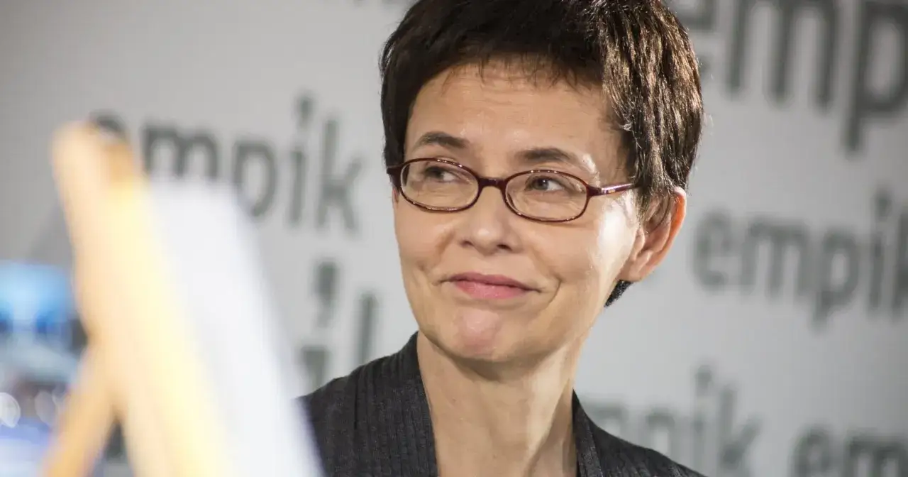 Uśmiechnięta Grażyna Jagielska w okularach, na tle napisu