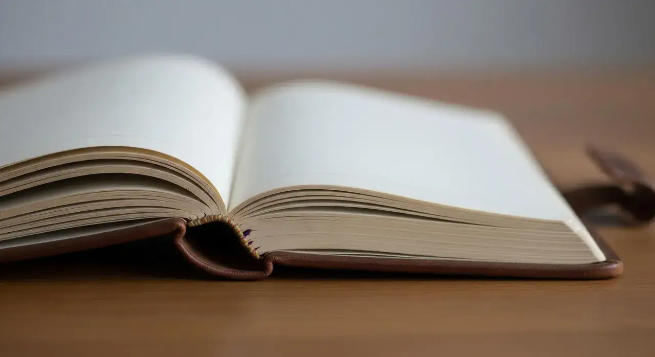 Otwarta, brązowa księga na drewnianym stole. Idealne miejsce na zapisanie najlepszych biografii.