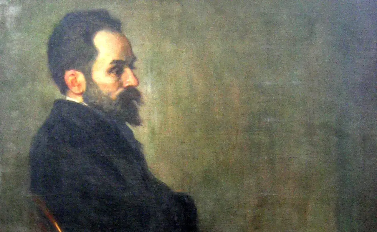 Portret Stefana Żeromskiego, pisarza o charakterystycznej brodzie i wąsach, w ciemnym stroju, na tle zielonej ściany.