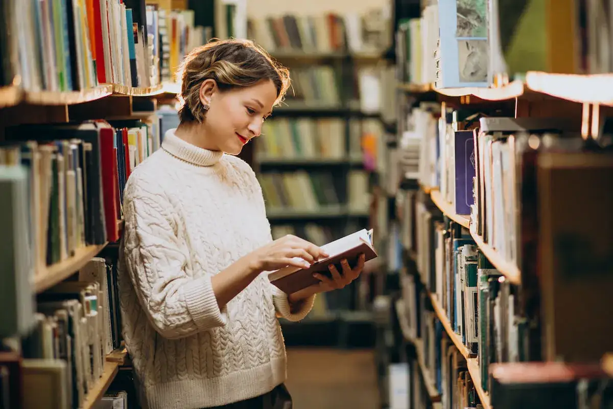 Kobieta w swetrze wybiera książkę w bibliotece, szukając inspiracji, jak zacząć czytać książki.